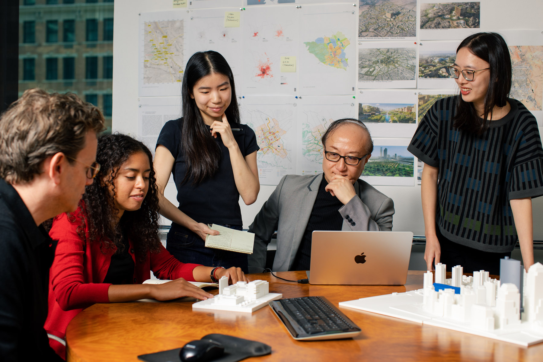 Design team reviewing architectural models and site maps during a studio meeting.